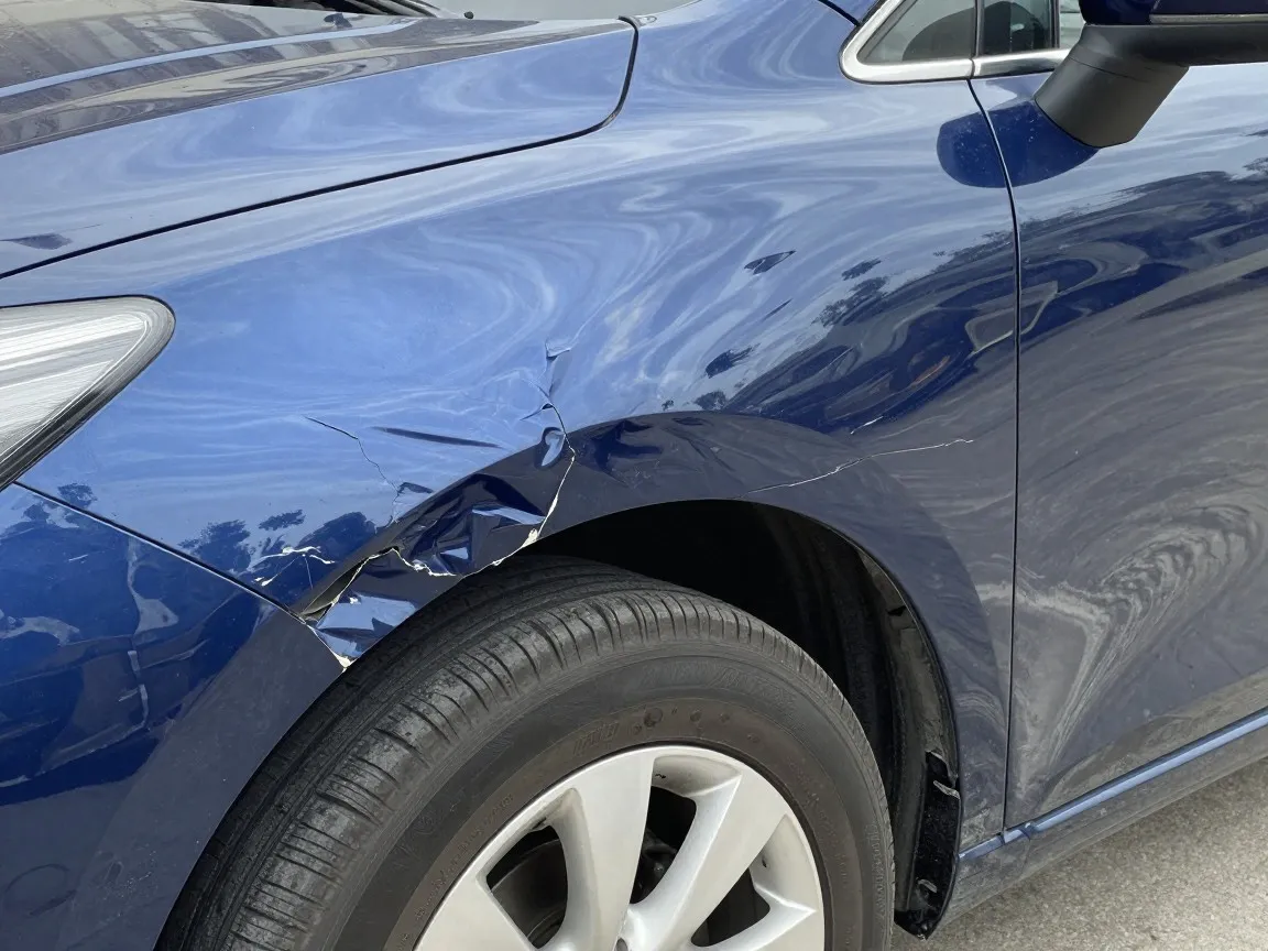 Blue front fender pushed in above the wheel, with buckled metal and cracked paint