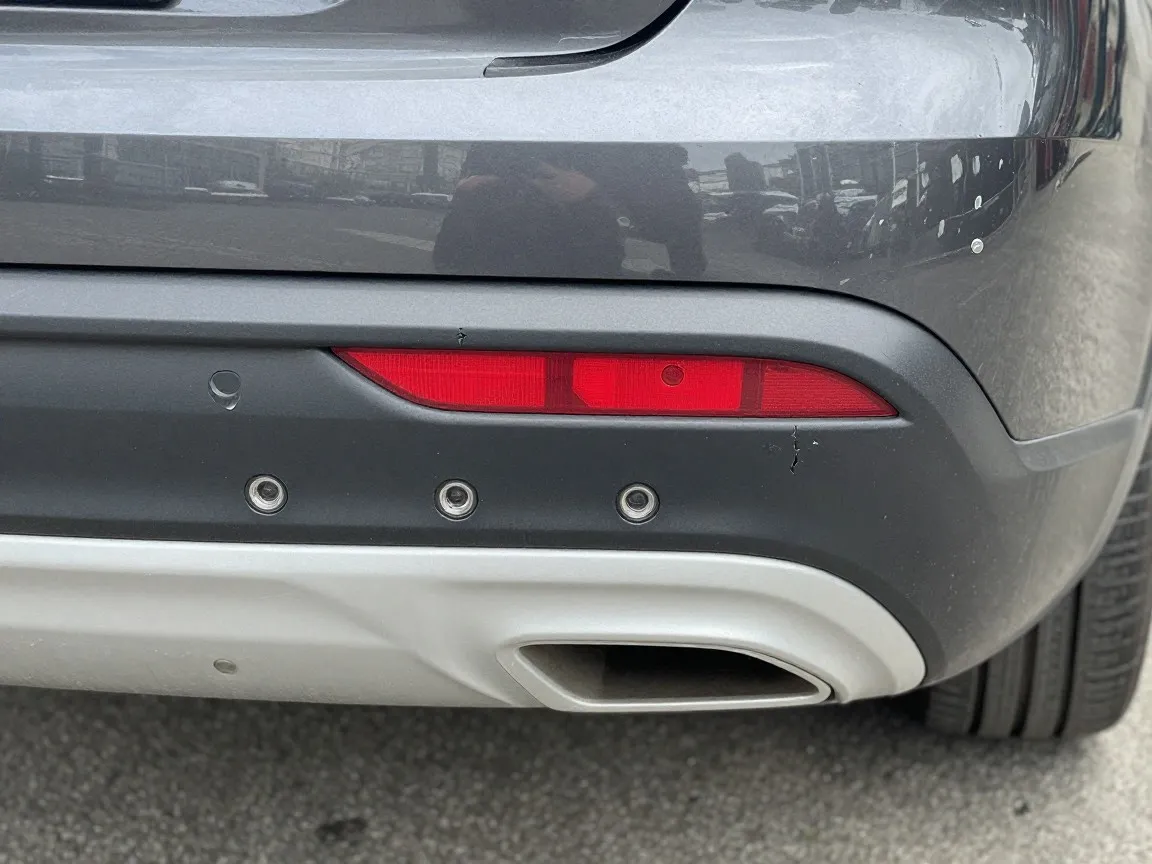 Rear bumper cover with round parking sensors set into the paint, scuffed and cracked near one sensor